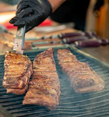 An individual is barbecuing ribs on a grill.