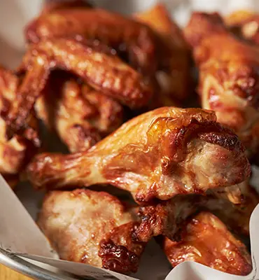 Savor delicious BBQ chicken wings served in a bowl, presented on a rustic wooden table.