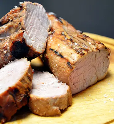 Savour deliciously grilled pork tenderloin, presented on a rustic wooden cutting board.