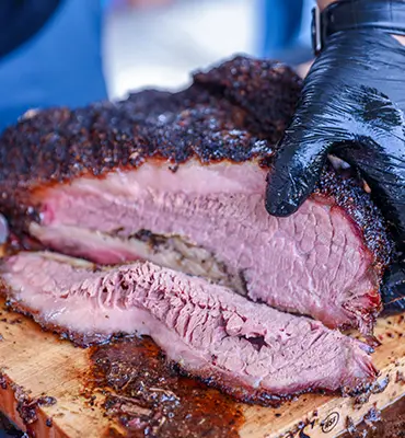 An individual is expertly slicing a succulent brisket on a robust cutting board.