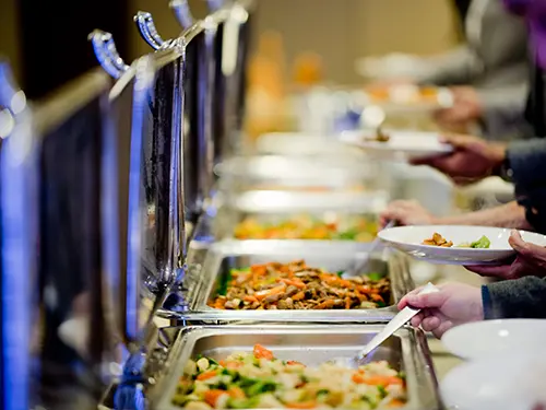 A team is dedicatedly catering at a buffet event, providing an array of delicious food options to guests.