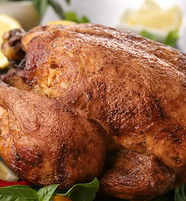 Close-up of a roasted chicken with crispy skin, surrounded by vegetables and garnish on a serving platter.